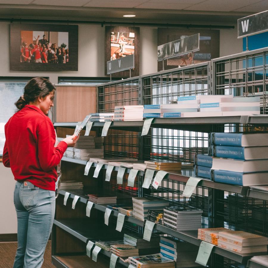 900x900 Student in bookstore next to a shelf of books looking at a book