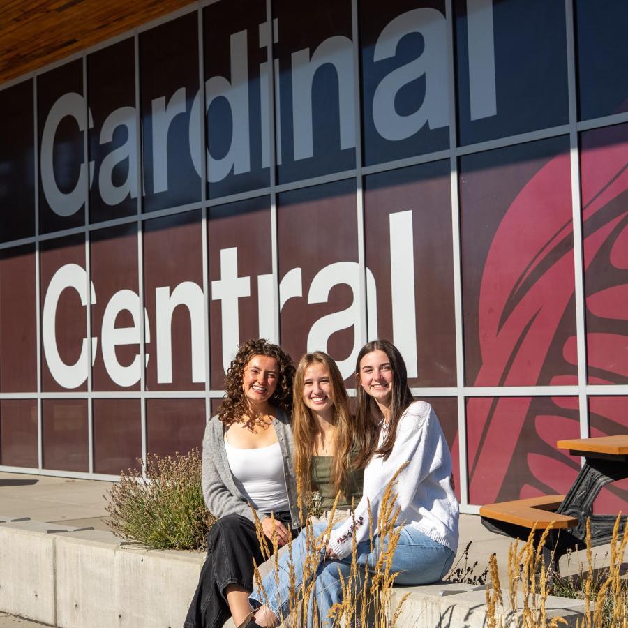 cardinal central side building outside, with 3 female student sitting