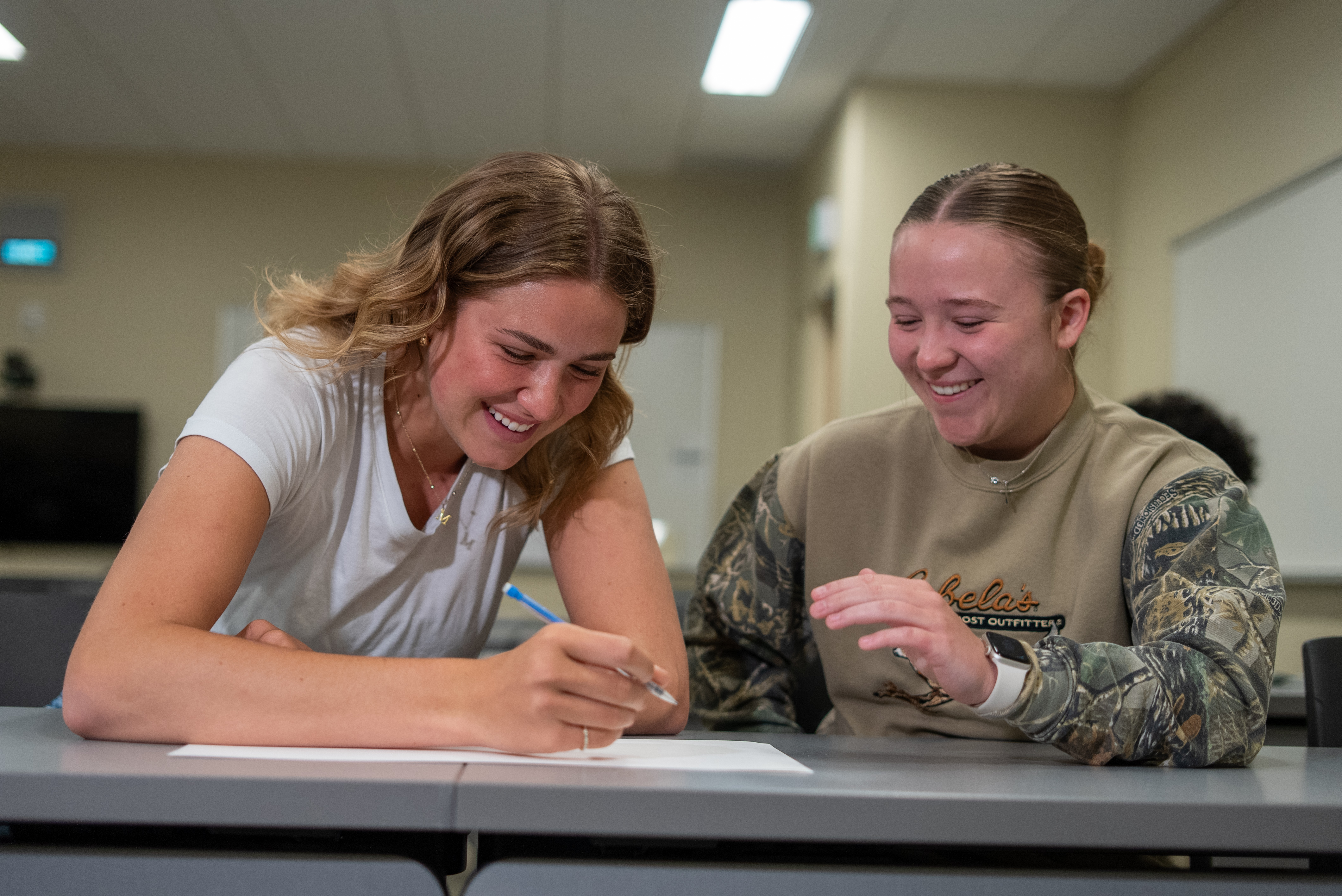 2 female students smiling at table together
