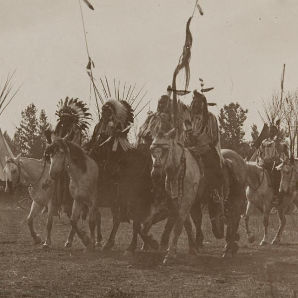 Native Americans wearing headdresses on horseback