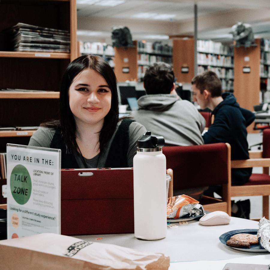 900x900 female student eating and studying in library