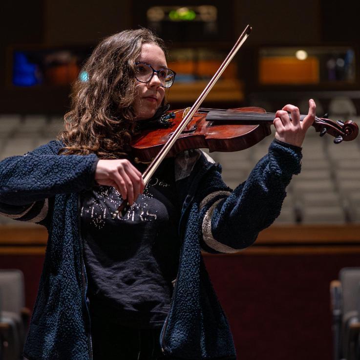 NIC female student playing the violin in theatre