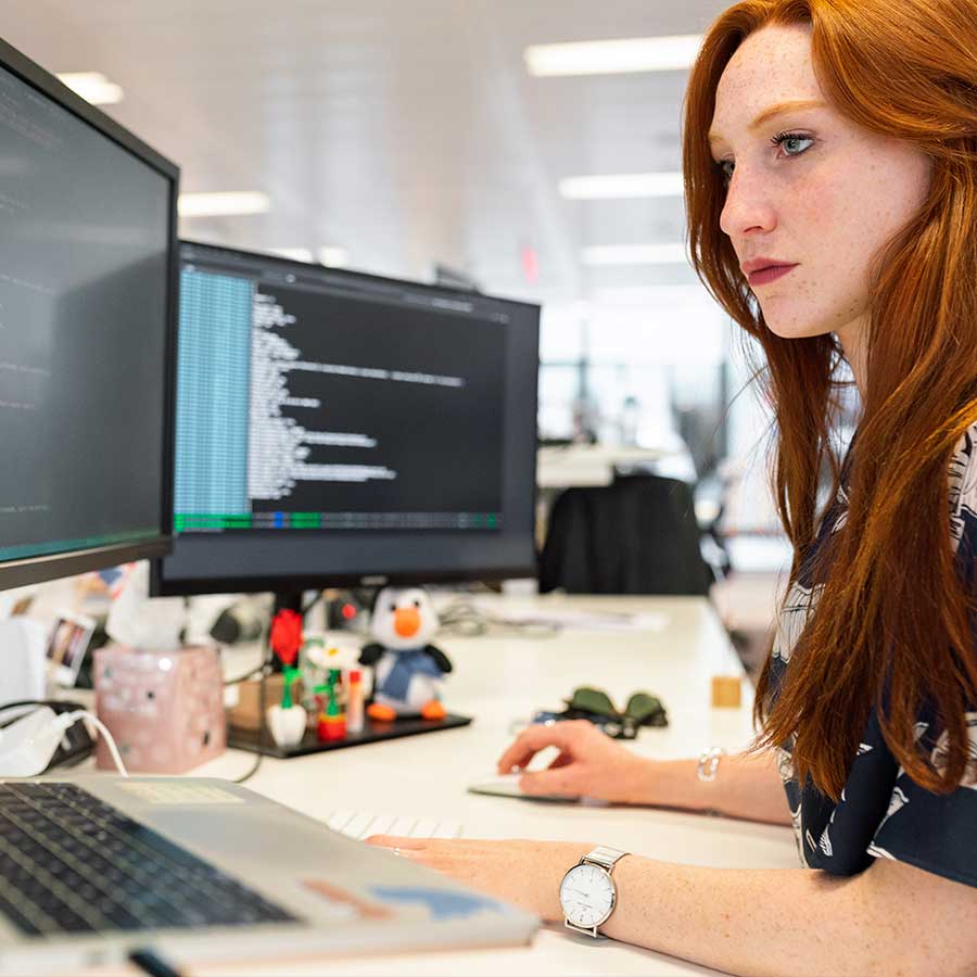 Young woman programming in front of multiple computer monitors